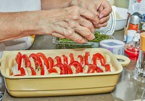 Chef puts tomatoes, potatoes and onions cut into circles in ceramic dish photo