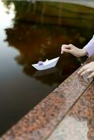 Paper boat made of paper, the boat goes on the water, a sprig of lilac on the boat, I launch the boat into the water photo