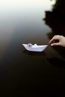 Paper boat made of paper, the boat goes on the water, a sprig of lilac on the boat, I launch the boat into the water photo