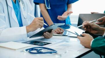 Medical team having a meeting with doctors in white lab coats and surgical scrubs seated at a table discussing a patients working online using computers photo