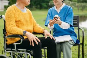 Asian careful caregiver or nurse and the happy patient in a wheelchair are walking in the garden. to help and encourage and rest your mind with green nature. Use a stethoscope to listen photo