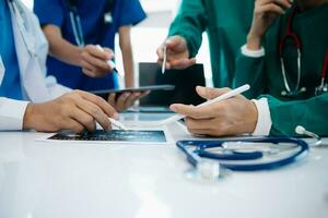 Medical team having a meeting with doctors in white lab coats and surgical scrubs seated at a table discussing a patients working online using computers photo