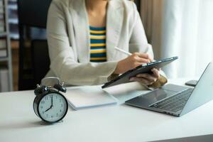 Alarm clock on the desk. Business hand using smartphone, laptop and tablet  working in modern office building photo