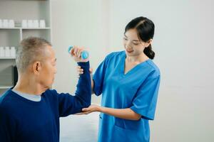 Asian physiotherapist helping elderly man patient stretching arm during exercise correct with dumbbell in hand during training hand with patient Back problems photo