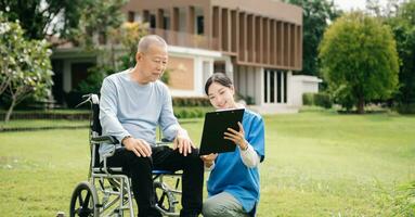 Asian careful caregiver or nurse and the happy patient in a wheelchair are walking in the garden. to help and encourage and rest your mind with green nature. Use a stethoscope to listen photo