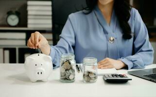 mujer de negocios sosteniendo monedas poniendo en vidrio usando un teléfono inteligente y una calculadora para calcular el concepto de ahorro de dinero para la contabilidad financiera foto