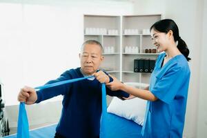 asiático fisioterapeuta Ayudar mayor hombre paciente extensión brazo durante ejercicio correcto con pesa en mano durante formación mano con paciente espalda problemas foto