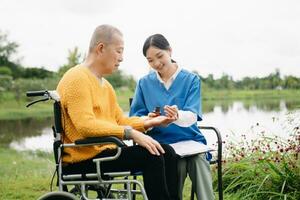 Asian young caregiver nurse support senior older male walking outdoors. Specialis doctor help and take care of elderly mature. Nursing home hospital garden photo