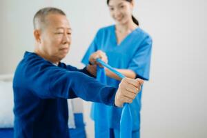 Asian physiotherapist helping elderly man patient stretching arm during exercise correct with dumbbell in hand during training hand with patient Back problems photo