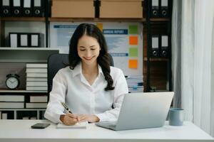 Asian businesswoman hand writing on the notepad with new modern computer strategy diagram as concept morning light photo