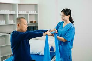 Asian physiotherapist helping elderly man patient stretching arm during exercise correct with dumbbell in hand during training hand with patient Back problems photo