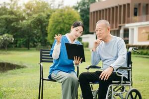 Asian careful caregiver or nurse and the happy patient in a wheelchair are walking in the garden. to help and encourage and rest your mind with green nature. Use a stethoscope to listen photo