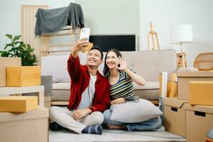 asiático joven atractivo Pareja hombre y mujer utilizar tableta y teléfono inteligente en línea compras mueble Decorar casa con caja de cartón paquete moverse en nuevo casa. joven casado Moviente hogar. foto