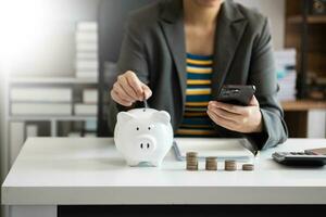 Business woman hand putting money coin into piggy bank with step of growing stack coins for saving money with virtual icon photo