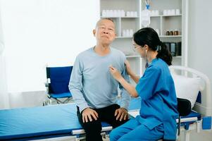 Asian doctor in white suit take notes while discussing and Asian elderly, man patient who lying on bed with receiving saline solution in hospital or clinic. photo