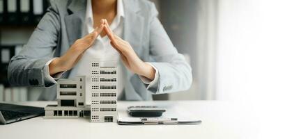 Female real estate agent is use hands to protect red roof for the concept of real estate investment about house trading, purchase at desk in office photo