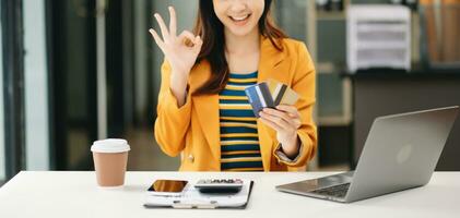 asiático mujer utilizando inteligente teléfono para móvil pagos en línea compras, omni canal, sentado en mesa, virtual íconos gráficos interfaz pantalla foto
