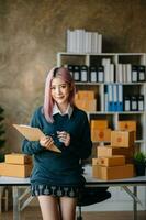 Young business owner woman prepare parcel box and standing check online orders for deliver to customer on tablet, laptop Shopping Online concept. photo