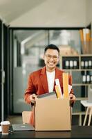 contento y emocionado joven asiático hombre oficina trabajador celebrando su resignación, que lleva su personal cosa. dejando trabajo, cambiando o empresa.en oficina foto