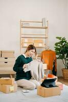 Portrait of Asian young woman SME working using smartphone or tablet taking receive and checking online purchase shopping order online concept. photo