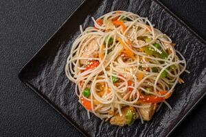 Tasty dish of Asian cuisine with rice noodles, chicken, asparagus, pepper, sesame seeds photo