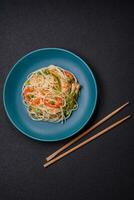 Tasty dish of Asian cuisine with rice noodles, chicken, asparagus, pepper, sesame seeds photo