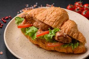 Delicious fresh crispy croissant with chicken or beef meat, lettuce, tomatoes, spices and sauce photo