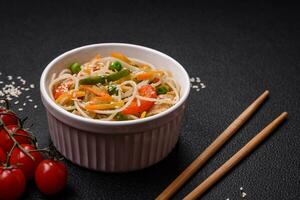 Tasty dish of Asian cuisine with rice noodles, chicken, asparagus, pepper, sesame seeds photo