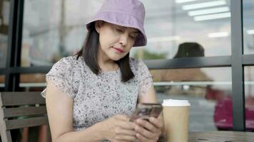 joven mujer sentado en un café tienda Bebiendo café y utilizando un teléfono inteligente durante un descanso en un estilo de vida café tienda video