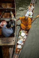 Ratchaburi Tailandia - enero12,2019 - tailandés monje recepción comida desde tailandés mujer ofrecimiento en dumneón Saduak canal uno de más popular de viaje destino en Tailandia foto