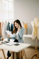 Asian tailor woman working on clothes in tailoring atelier. beautiful young female fashion designer smile and after success in modern tudio photo