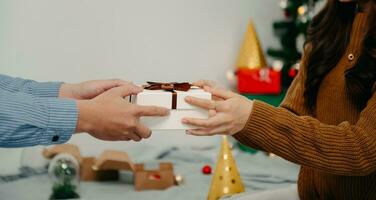 Christmas Gift in hands. Happy Man giving Christmas and New Year Gift box to woman at Home. Family Xmas celebration. Christmas decoration. photo