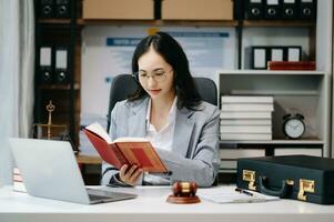 Asian Woman lawyer reading legal book with gavel on table in office. justice and law ,attorney concept. photo