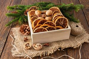 Square wooden box with dried orange slices and walnuts on burlap and rustic table with green spruce branches. Eco Christmas style. photo