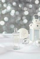 New Year's fragrance. Beautiful perfume bottle on white satin background with christmas decorations and bokeh light effect. Vertical front view. photo