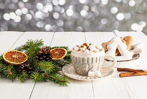 The mood of Christmas morning. Cup with New Year knitted hot chocolate pattern with marshmallow, gingerbread with icing on wooden white table. photo