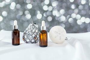 Two cosmetic bottles with a dropper with a natural skin care product for the face against the background of Christmas balls. effect of bokeh light. photo