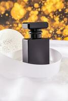 Elegant black matte bottle with cosmetic men's product or perfume with white ribbon and christmas ball. Golden bokeh light effect. photo