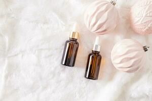 Two cosmetic bottles with dropper with natural self-care product on white fur background with elegant christmas balls. A copy of the space. photo