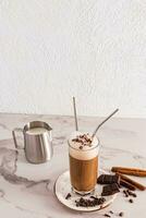 A tall glass with a chocolate drink with cinnamon and pieces of chocolate stands on a plate and a marble table. coffee latte, urine. Delicious drink photo