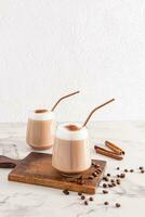 Two chic glasses with cappuccino coffee or cinnamon latte a delicious with eco straw on a wooden cutting board. Front vertical view. A copy space. photo