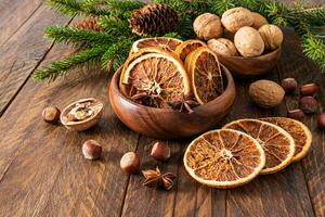 Two wooden bowls with dried orange slices and walnuts on a wooden table with spruce branches. Preparing Christmas decor in the village. photo