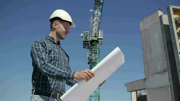 Builder stands with set of plan at the bulding under construction video