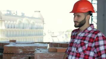 männlich Baumeister korrigiert seine schwer Hut beim das Gebäude unter Konstruktion video