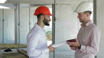 Two builders looking at the digital tablet at the building under construction video