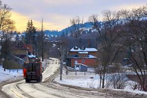 A truck collecting garbage drives through an evening winter town photo