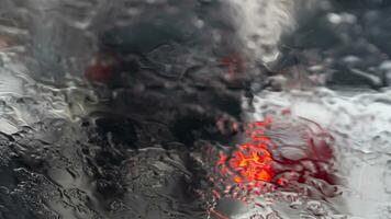 Abstract of rain move on the fron glass of car. Blurred of the rear side cars with red light from brake. Environment at rainy time on the road. photo