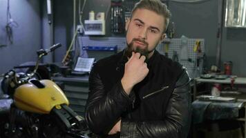 Male biker scratches his beard at the motorcycle workshop video