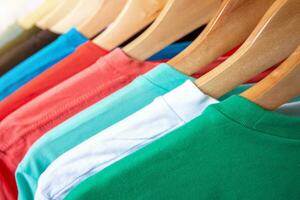 Fashion T-shirt on clothing rack - Closeup of bright colorful closet on wooden hangers in store closet. photo