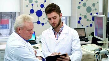 Male scientist shows something on his tablet to his coworker at the laboratory video